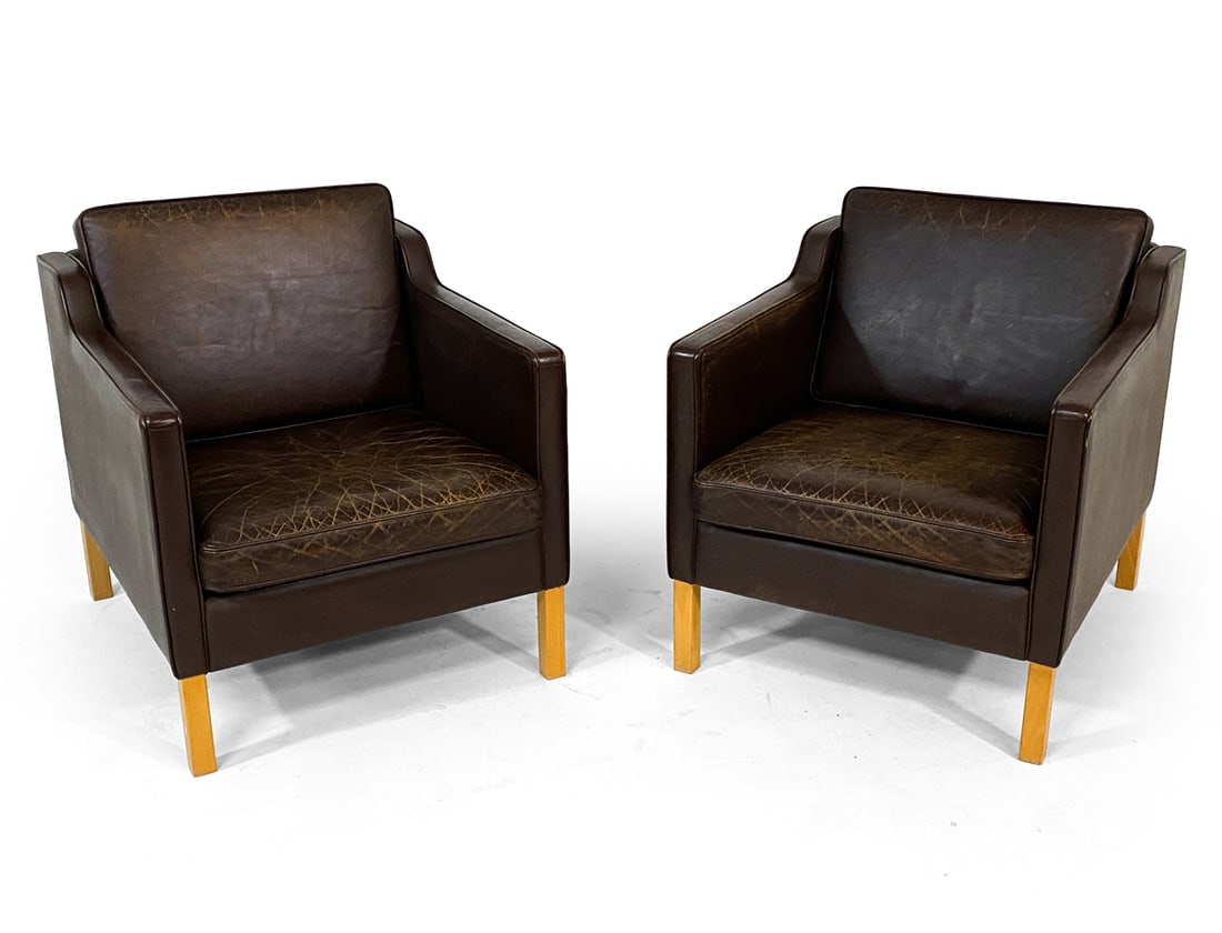 PAIR ATTR. STOUBY DANISH LEATHER LOUNGE CHAIRS: Brown leather upholstery with beech legs. Denmark, circa 1960s. Dimensions: H 28" x W 31" x D 31" x SH 16.5". Condition: Scuffs and scratches to leather, some drying notable to cushions and arms. Wear