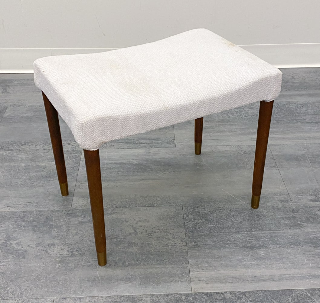 DANISH BEECH OTTOMAN FOOTSTOOL C. 1960S: Ottoman with white fabric upholstered seat. Tapered beech legs with brass caps. Denmark, circa 1960s. Dimensions: H 17" x W 19" x D 13.5". Condition: Slight discolored spots to fabric. Wear consistent