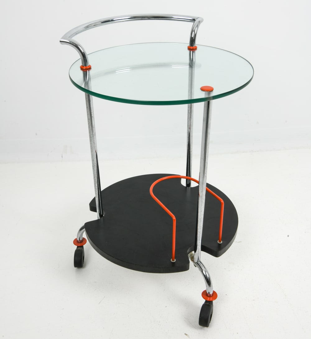 METALNOVA ITALIAN GLASS & CHROME BAR CART: Chromed steel frame, a top glass shelf, and a lower shelf in black lacquered wood. Red metal details to surface and the curved holder on the bottom shelf. Marked to metal part above rolling casters. L