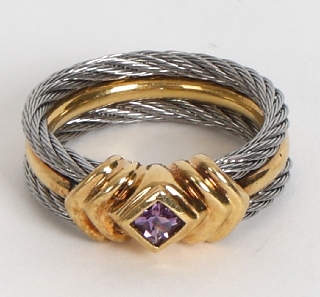 18K GOLD, STAINLESS & AMETHYST RING: Gold ring with thin steel cables woven into band. Set with amethyst stone. Marked to band. Dimensions: Ring Size 6. Condition: Faint rubs. Wear consistent with age and use.