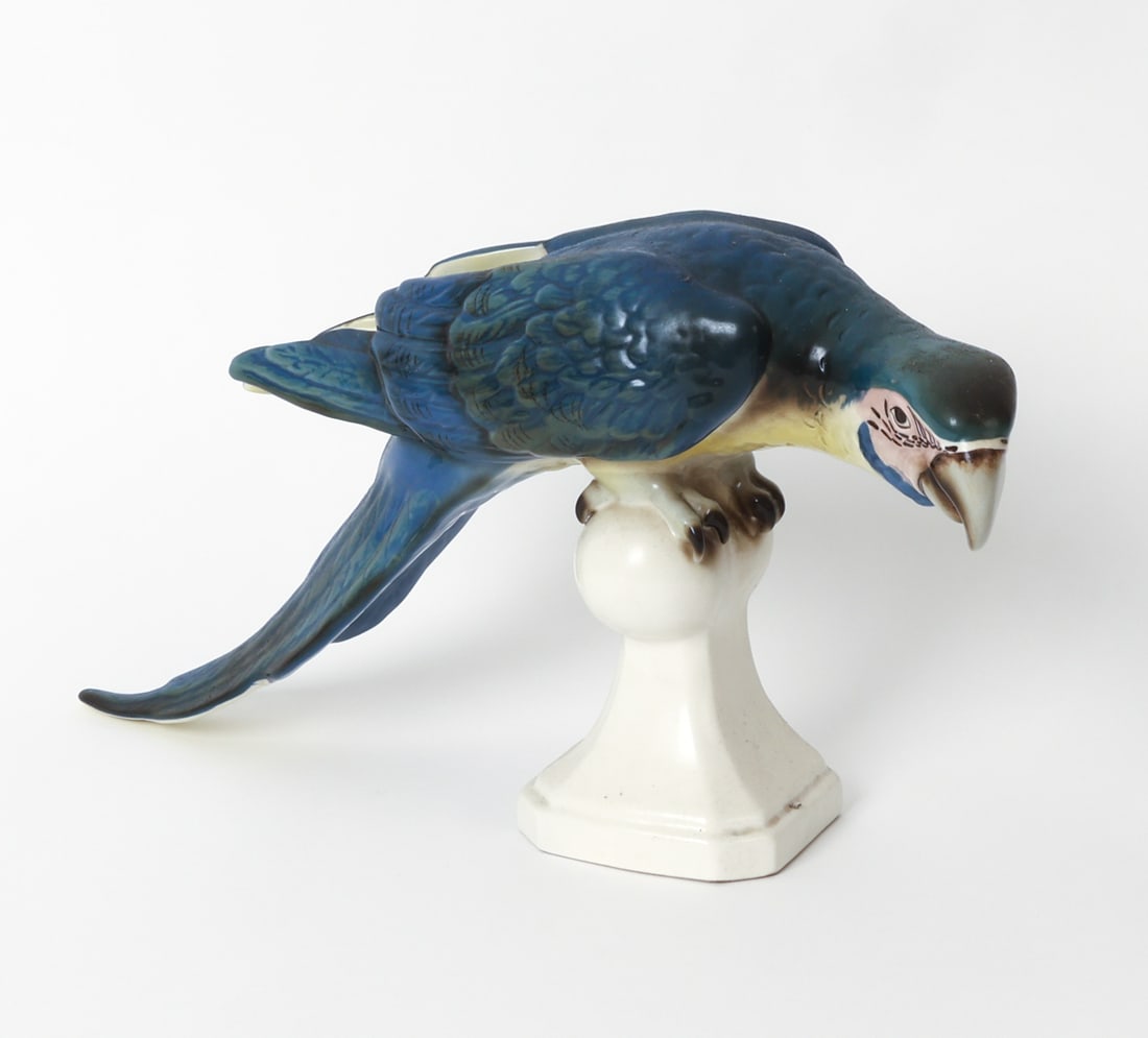 ROYAL DUX PORCELAIN MACAW PARROT FIGURE: Marked underneath. Porcelain ceramic macaw with blue plumage. 20th century. Dimensions: H 9" x W 6" x D 16.5". Condition: Wear consistent with age and use as displayed.