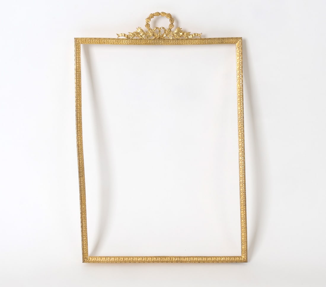 FRENCH EMPIRE GILT BRONZE PICTURE FRAME: Gilded bronze picture frame with laurel wreath and ribbon crest at top. Dimensions: H 15.25" x W 10.5". Sight H 12.75" x W 19.25". Condition: Slightly bent. Light scuffs and rubs. Wear consistent with