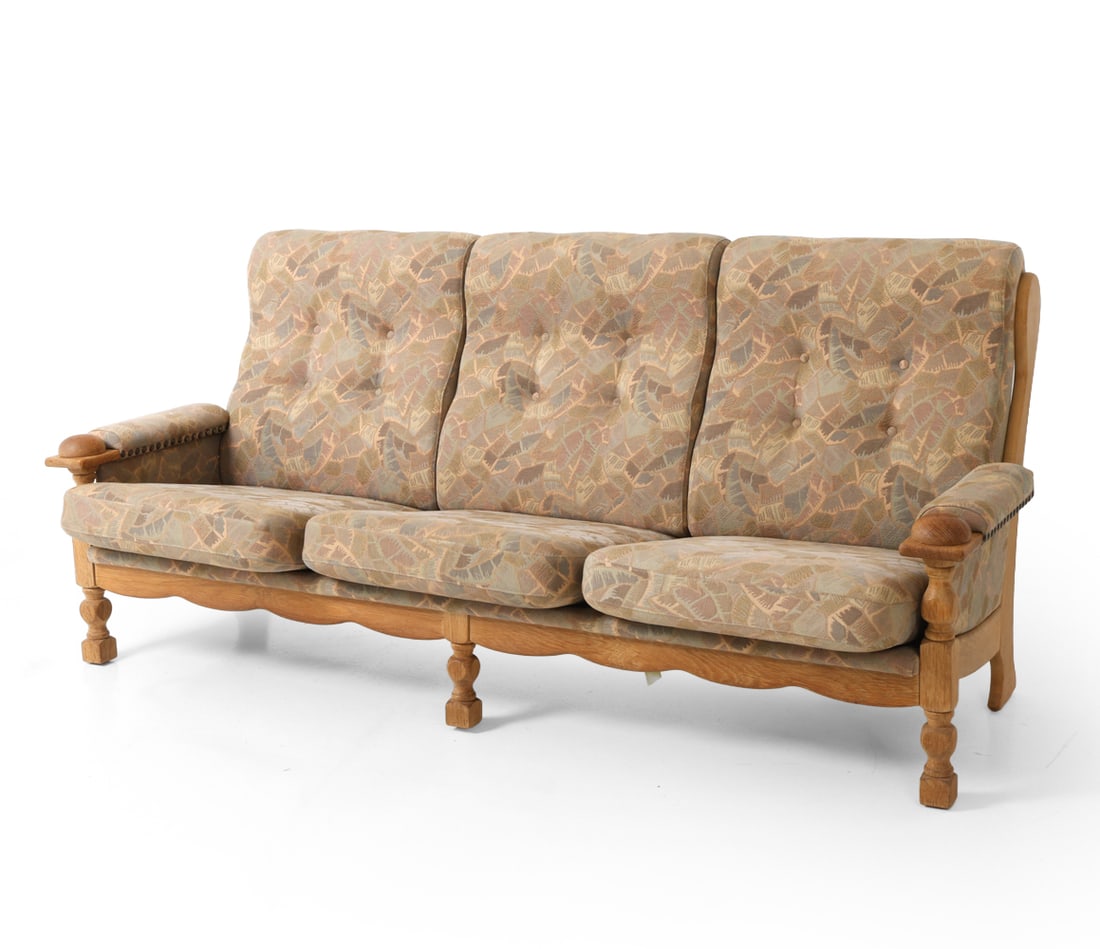 STYLE OF KJAERNULF DANISH OAK SOFA C. 1970S: Three-seater brutalist sofa with scalloped ladder back and turned legs. Roundels at the arm terminals. Pattern upholstered cushions with brass details to armrest. Denmark, circa 1970s. Dimensions: H 3
