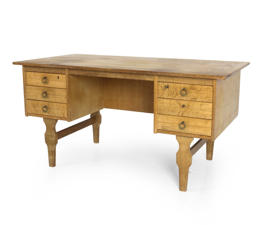 ATTR. HENNING KJAERNULF DANISH OAK WRITING DESK: Key included. Brutalist oak desk with carved legs and brass pulls. Apparently unmarked. Denmark, circa 1960s. Dimensions: H 29" x W 58" x D 29.5" Condition: Missing pull to right drawer. Marks to