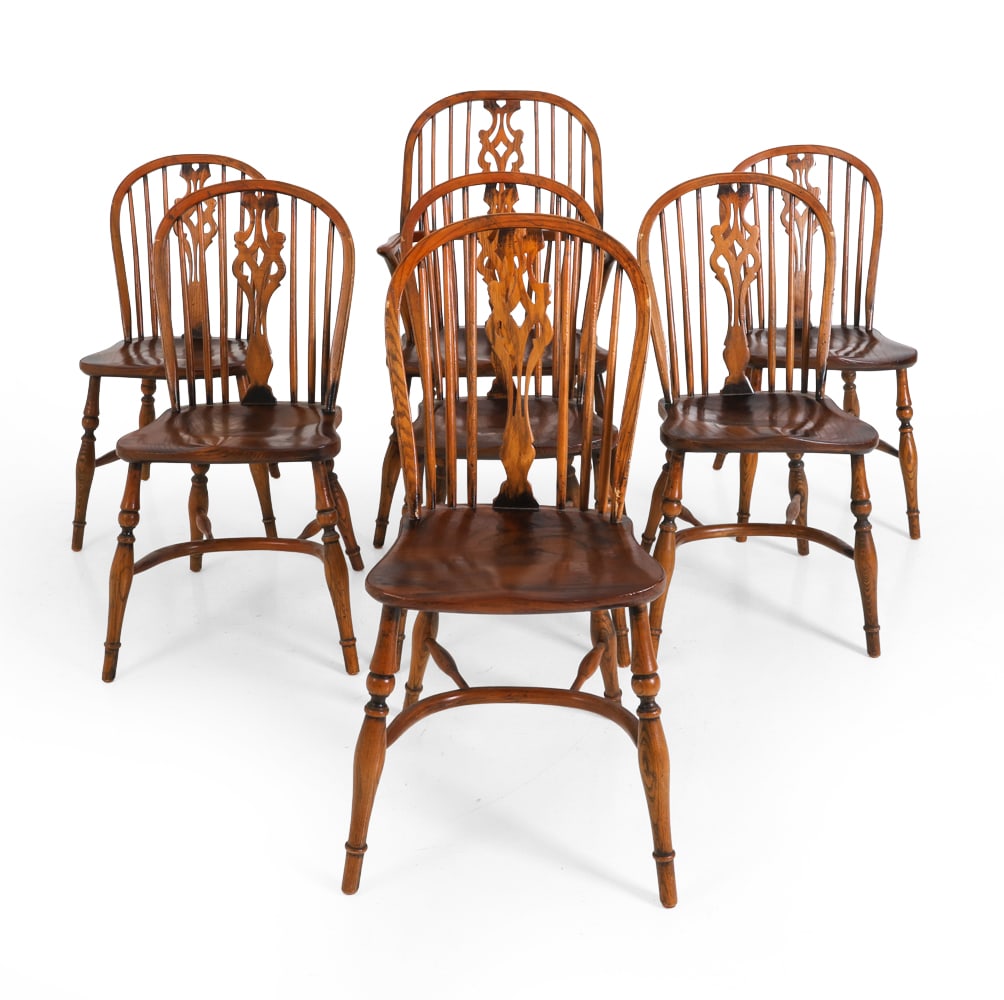 (7) ANTIQUE ENGLISH OAK WINDSOR CHAIRS C. 1920S: (7) Windsor wheelback chairs in oak with spindles back and carved central splat. One armchair and six side chairs. Splayed baluster legs connected by curved H-form stretcher. England, circa 1920s. Dim