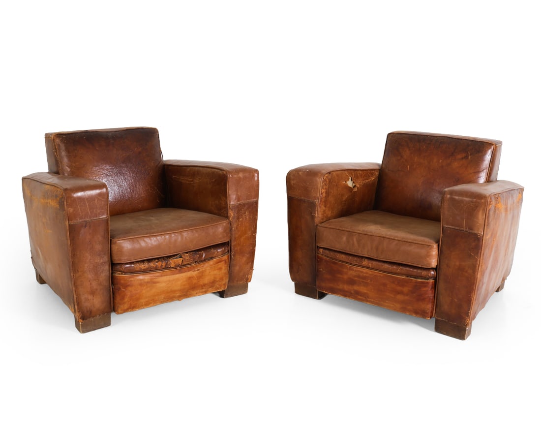 PAIR OF FRENCH ART DECO LEATHER CLUB CHAIRS: Two club chairs in brown leather upholstery. Oak legs. Brass tacks accents. 20th century. Dimensions: H 28.25" x W 35.5" x D 32.5" x SH 16". Condition: Scratches, rubs, and fading with tears to leathe