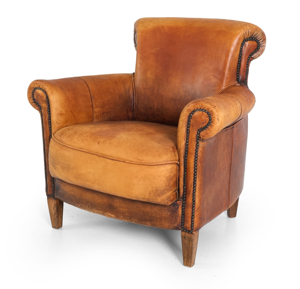 ENGLISH STYLE DISTRESSED LEATHER CLUB CHAIR: Brown leather club chair with brass tacks and rolled arms and back. Oak legs. 20th century. Dimensions: H 33" x W 32.5" x D 27.5" x SH 17.5". Condition: Drying and flaking to leather with large tear t