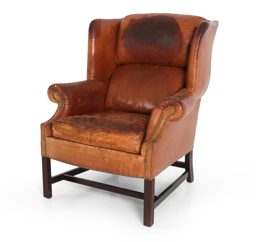 GEORGIAN STYLE LEATHER WINGBACK LOUNGE CHAIR: Brown leather upholstery with beech feet. 20th century. Dimensions: H 40.5" x W 34" x D 33" x SH 19.5". Condition: Heavy discoloration and drying to leather with few tears. Wear consistent with age an