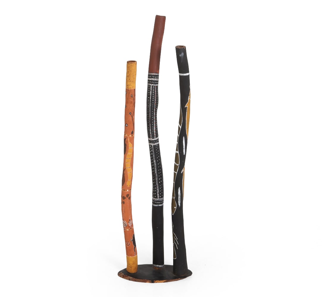 PAINTED DIDGERIDOO GROUPING: Three painted didgeridoo instruments with custom stand. 20th century. Dimensions: Tallest H 51.5". Condition: Scuffs and rubs to painted finish.
