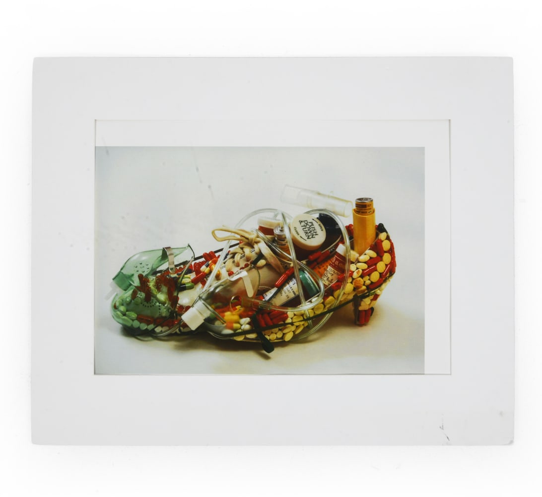 NINA BENTLEY (B. 1939) SHOE PHOTO PRINT: Titled 'Till Death Do Us Part' to lower left, and signed to lower right corner. Photograph featuring pills and medical equipment wrapped up in a lady's shoe. Dimensions: H 25" x W 35.75". Sight H 16.2