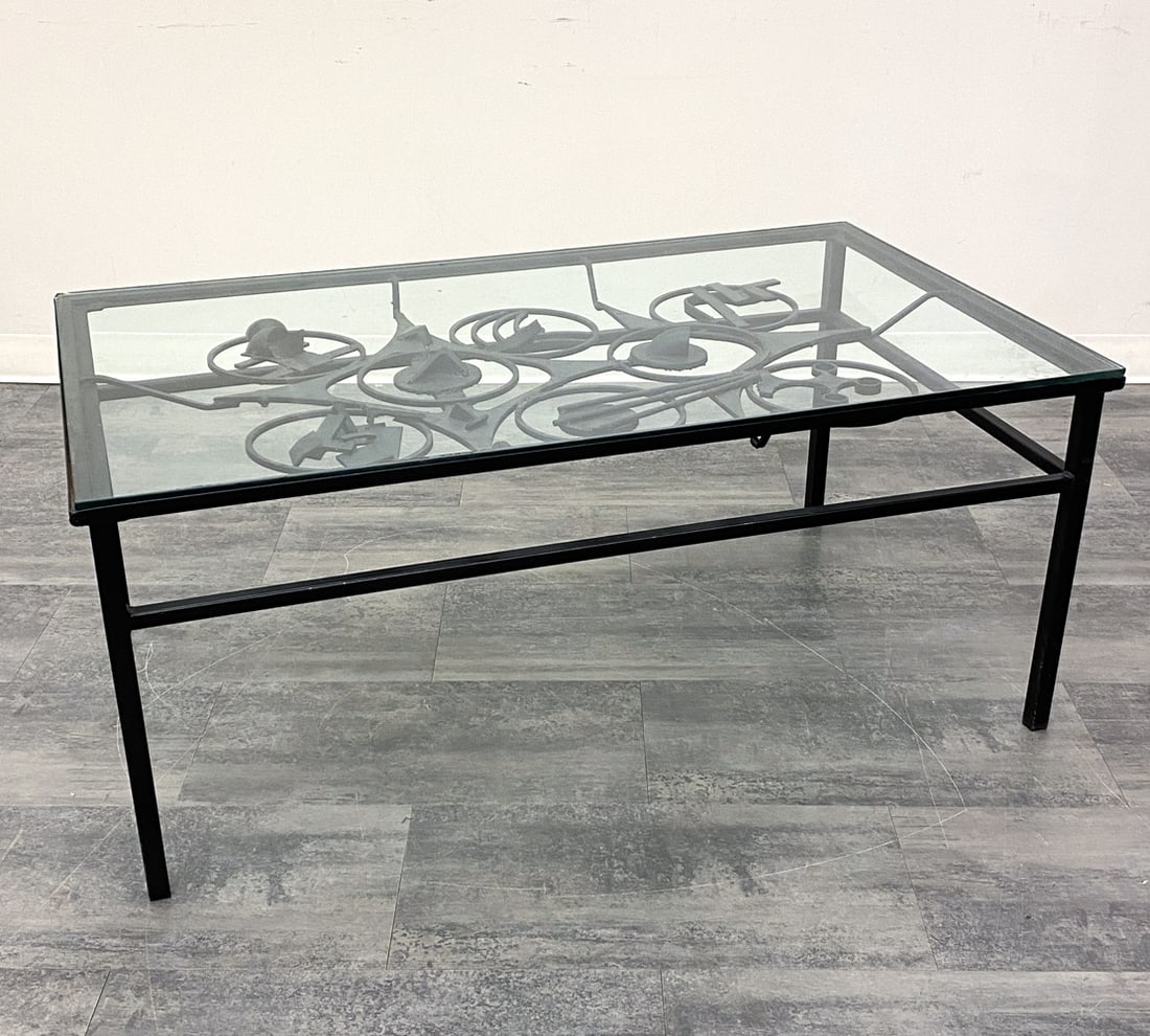 WELDED SCULPTURAL IRON & GLASS COFFEE TABLE: Iron table base with abstract design. Glass top. Circa 1970s. Dimensions: H 21" x W 49.5" x D 29.75". Condition: Chip to corner of glass. Thin surface scratches. Wear consistent with age and use.