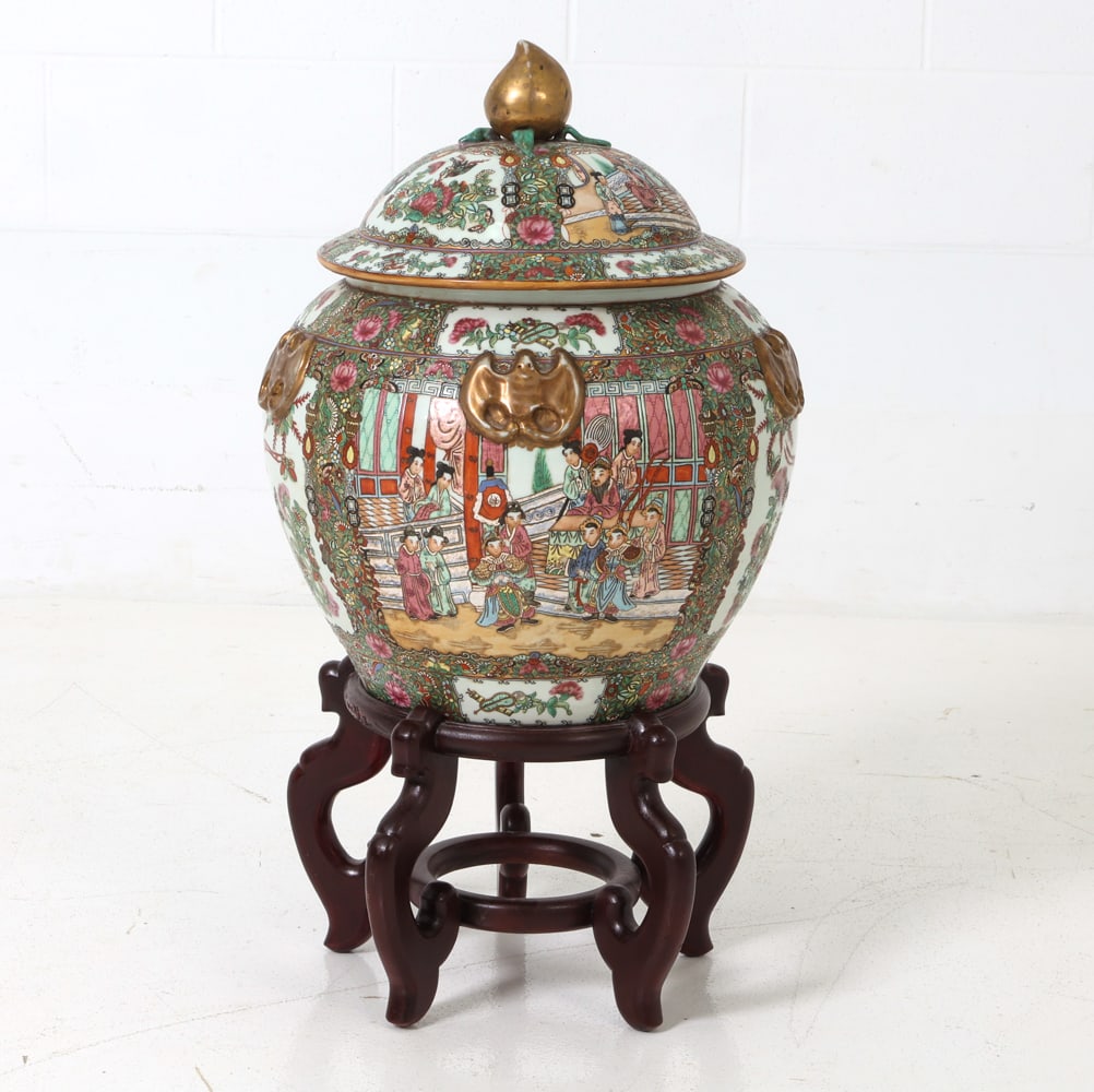 CHINESE ROSE MEDALLION PORCELAIN URN ON STAND: Chinese Famille Rose porcelain jar with lid on wooden stand. Featuring ornate panels depicting courtly figures, decorated with bats and floral motifs, and topped with a peach-shaped finial. Date of Ac