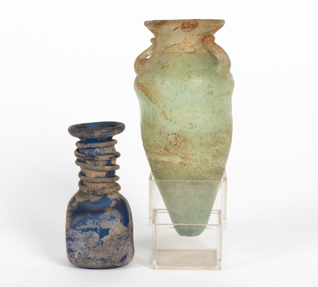 ANCIENT ROMAN IRIDESCENT GLASS VESSELS: Includes a larger green glass urn-form vessel and a smaller blue glass vessel. Dimensions: (Larger) H 5.5" x Dia 2.75" Condition: Burial remains, green vessel with roughness to bottom.
