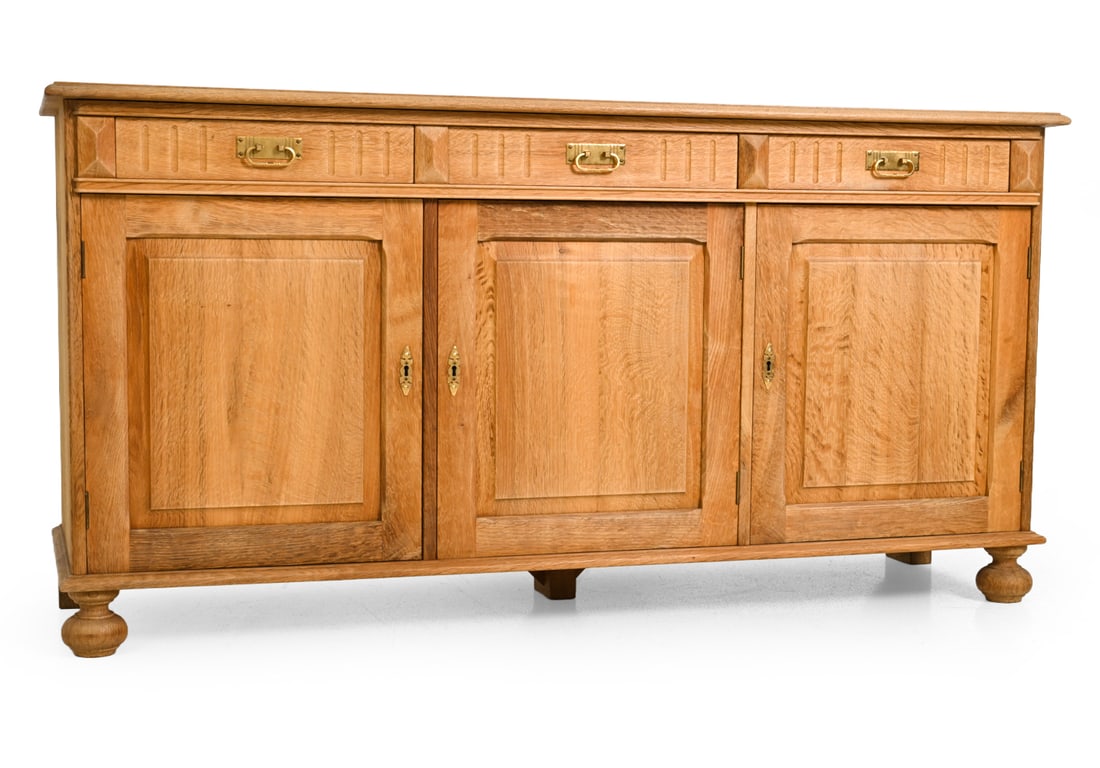 KJAERNULF STYLE DANISH OAK SIDEBOARD C. 1970S: Includes key. Carved oak with brass hardware. Denmark, circa 1960s. Dimensions: H 32" x W 62" x D 19.25" Condition: Some fading and discoloration to top. Drawers swollen slightly, Wear consistent