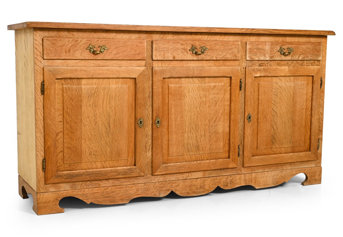 HUNDSTRUP DANISH OAK SIDEBOARD C. 1970S: Apparently unmarked. Key included. Carved oak with brass hardware. Denmark, circa 1970s. Key included. Three-door sideboard with drawers and brass pulls. Marked to back. Denmark, circa 1970s.