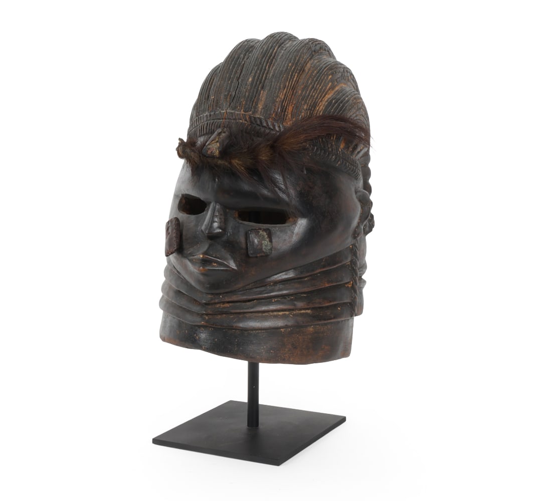 SIERRA LEONE VAI HELMET MASK: Mask is for a female elder to dance in the Sande Women's society. Features an animal tail brow nailed to mask. Sitting on metal stand. Dimensions: H 17.5" x W 8" x D 10" Condition: Lacking one nail to