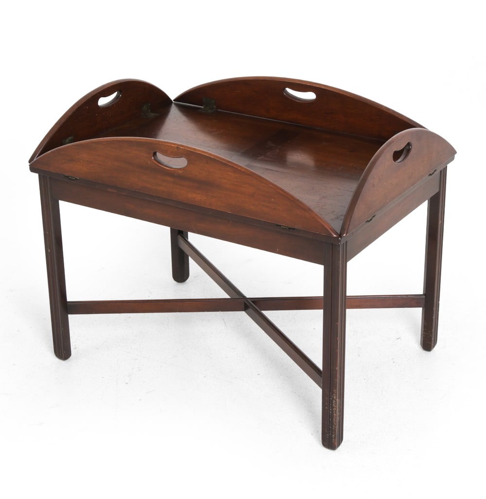 CHIPPENDALE-STYLE MAHOGANY FOLDABLE BUTLERS TABLE: Mahogany with foldable edges, carved legs, and brass hardware. Early 20th century. Dimensions: H 18.75" x W 39.5" x D 29.75" Condition: Scuffs, dings, discoloration, and wear to finish. Two holes on t