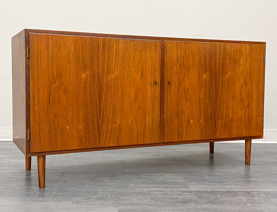 CARLO JENSEN FOR POUL HUNDEVAD ROSEWOOD CABINET: Two-door cabinet. Includes key. In rosewood. Apparently unmarked. Denmark, circa 1960s. Dimensions: H 27" x W 52" x D 18" Condition: Wear consistent with age and use. Fading, scuffs, nicks, minor ding