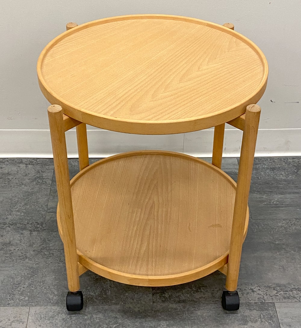 STYLE OF HANS BOLLING DANISH TRAY TABLE C. 1970S: Removable circular tray shelves and casters. In beech. Denmark, circa 1970s. Dimensions: H 22.5" x Dia 20" Condition: Wear consistent with age and use. Minor fading, scuffs.