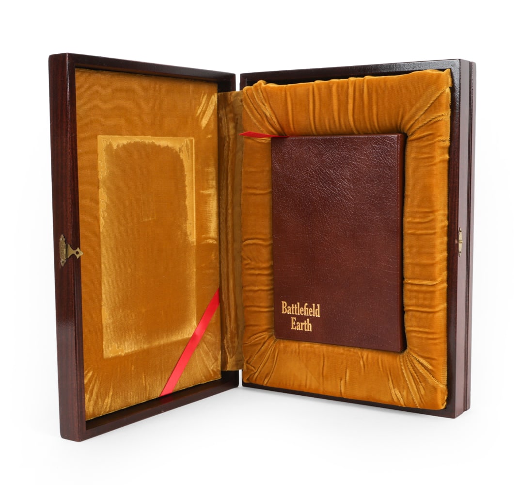 L. RON HUBBARD LIMTED EDITION BATTLEFIELD EARTH: Walnut case with plaque inscribed with "Battlefield Earth, Limited edition, Number 123 of 555". Interior has velvet lined pillow that holds leather bound book. 20th century. Dimensions: H 3.5" x W 16"