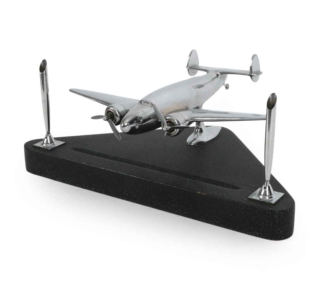 ART DECO CHROME PLANE PEN HOLDER: Chrome plated aluminum plane on wooden base. Features horizontal and pair of vertical pen holders. Rotating propeller blades. Provenance: Originally purchased at Bizarre Bazaar in 2000 for $850. Dimen