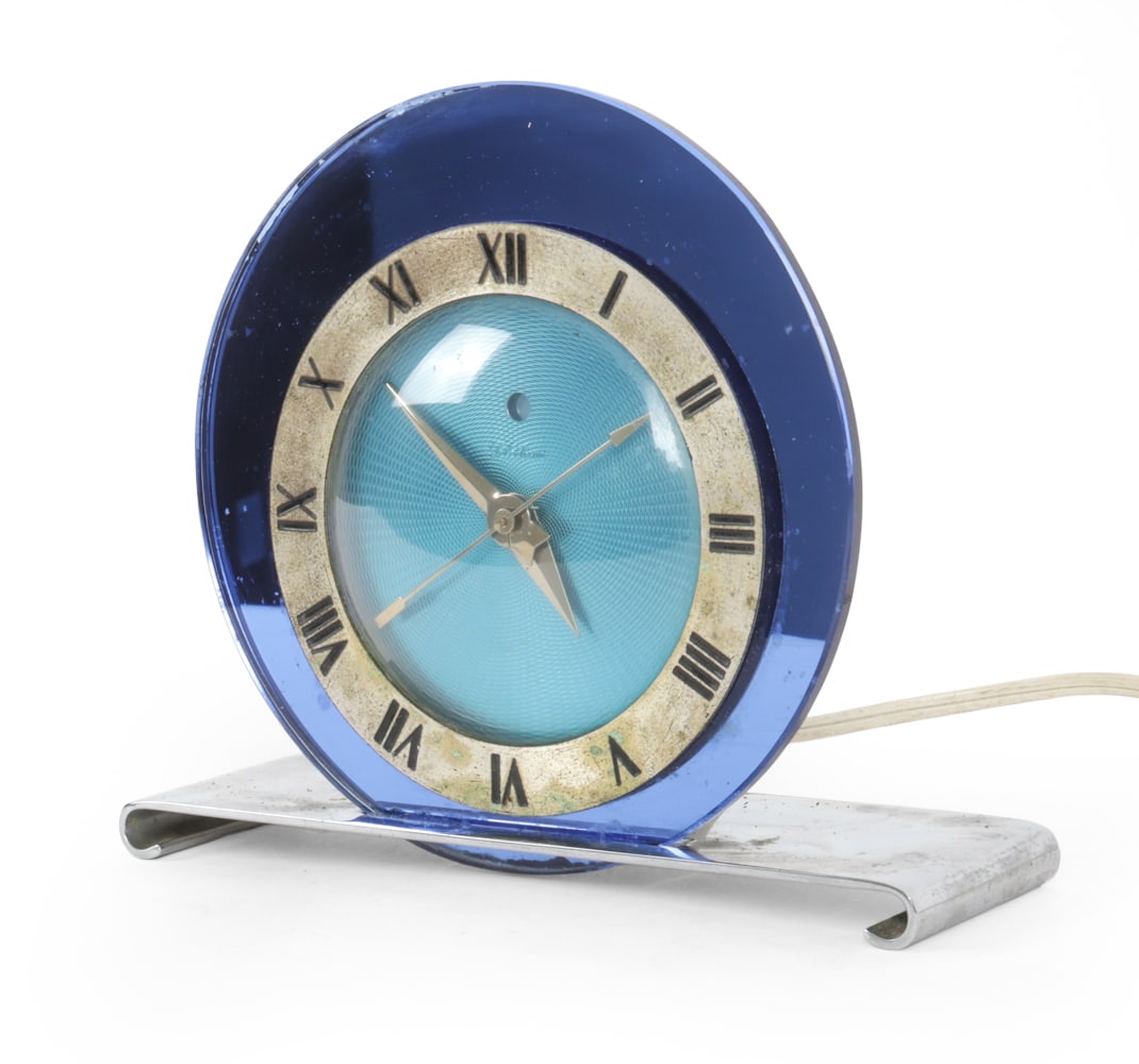 TELECHRON ART DECO BLUE MIRRORED CLOCK: Warren Telechron Co. Art deco electric clock, circa 1930s. Round blue mirrored glass with roman numeral dial on chrome base. Labeled verso. Dimensions: H 6.25" x W 7.25" x D 2.75" Condition: Showing s