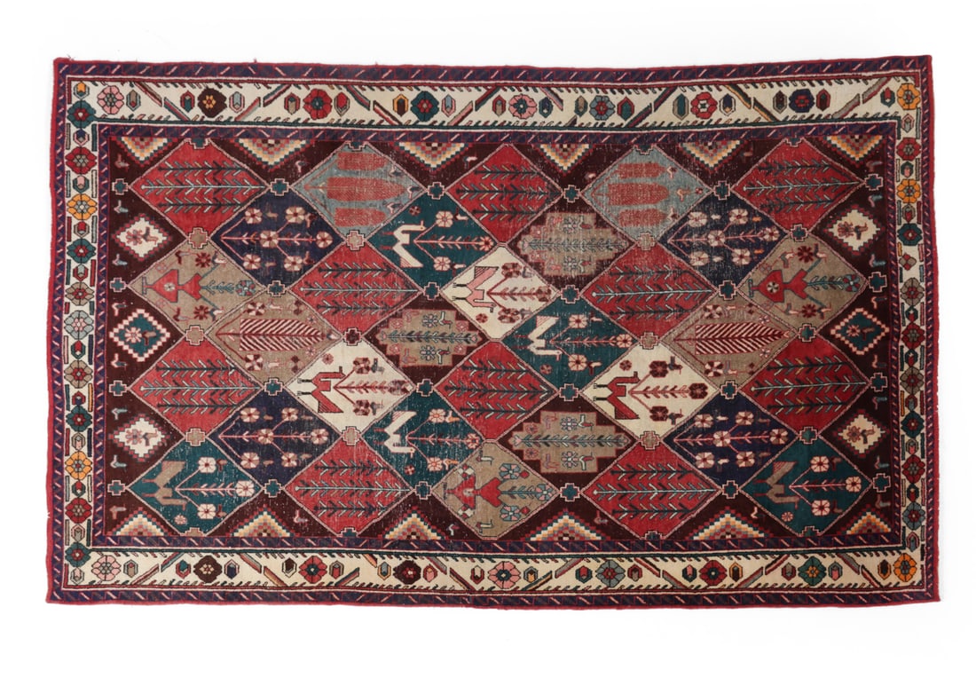 PERSIAN WOVEN WOOL RUG C. 1920S: Woven geometric design with nature motifs and fringe around edges. Wear consistent with age and use. Dimensions: L130 " x W 80.5" Condition: Loss of pile, loss of fringe, sun fading, moderate wear,