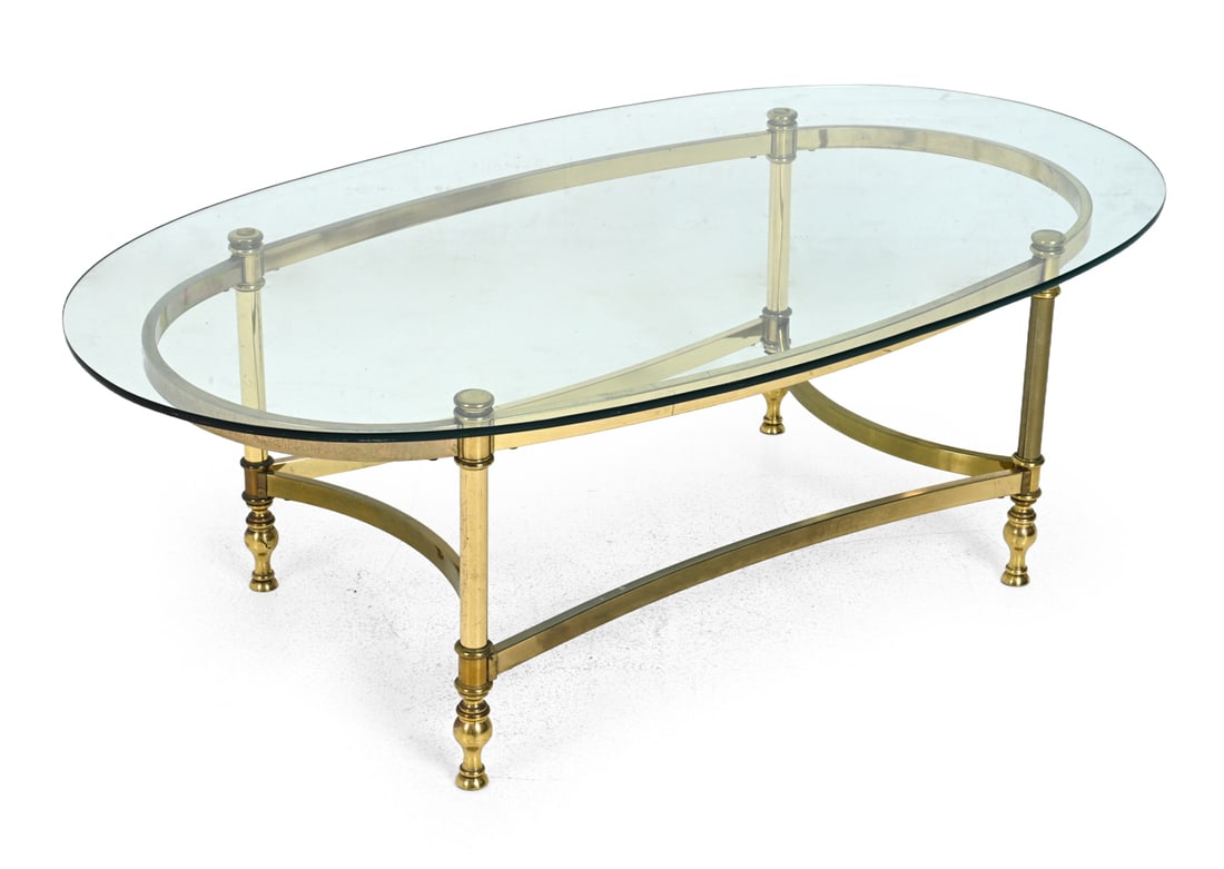 HOLLYWOOD REGENCY STYLE BRASS COFFEE TABLE: Plated brass base with turned legs. Glass top. Circa 1970s. Dimensions: H 16" x W 49" x D 27.25" Condition: Patina to base. oxidation. Scuffs to glass top. Hardware needs tightening. Wear consistent
