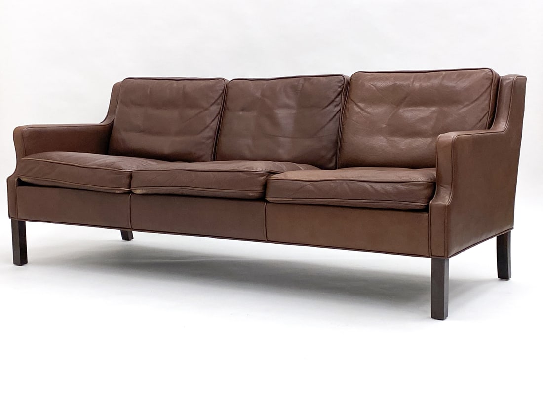 MID-CENTURY BORGE MOGENSEN STYLE LEATHER SOFA: Deep brown leather 3-seat sofa with oak legs. Dimensions: H 29.5" x W 73.5" x D 29" x SH 15" Condition: Faint tobacco odor. Tear to underlining on bottom. Some scuffs and discoloration to leather.