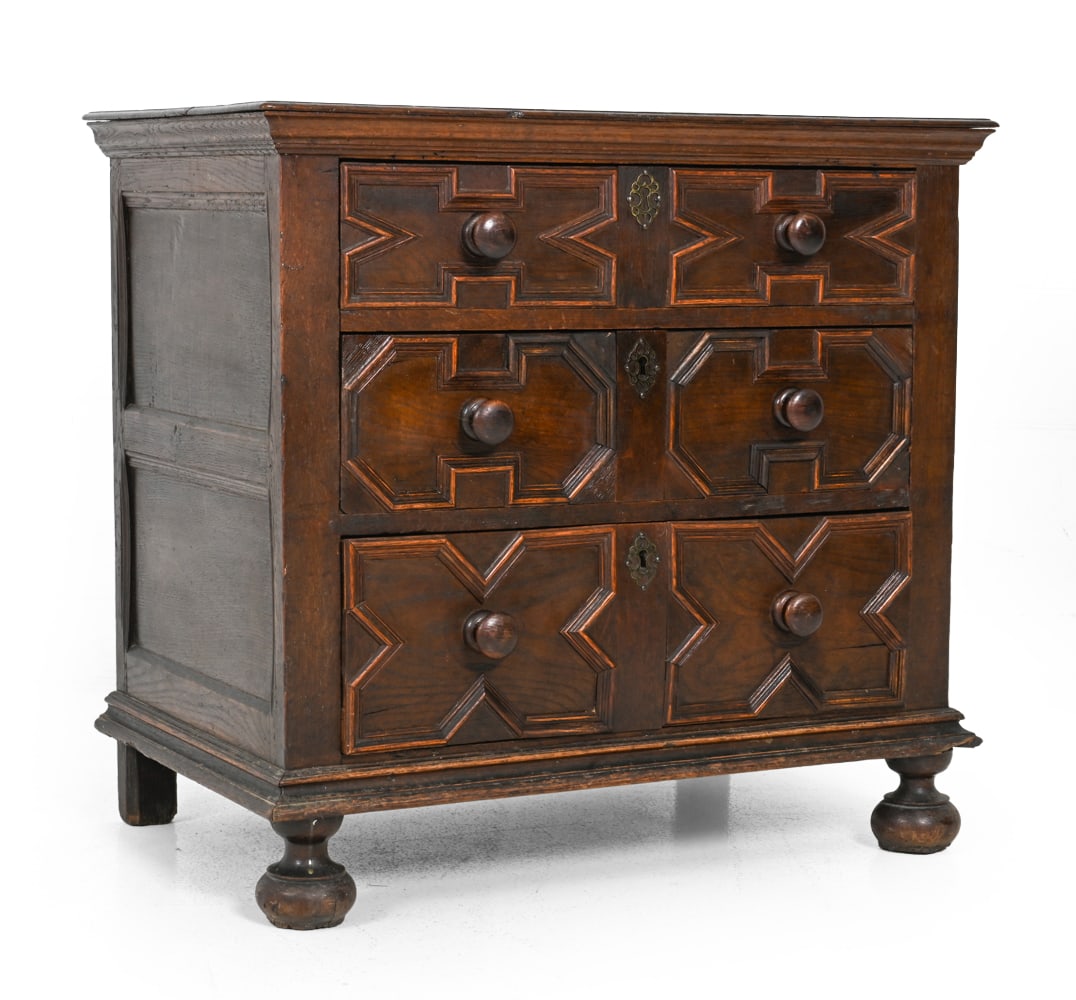 ENGLISH JACOBEAN STYLE OAK CHEST OF DRAWERS: Antique oak chest of drawers with bun feet, side hung drawers, and rose head nails. Brass keyholes and geometric panel moldings. England, Late 17th to early 18th century. Dimensions: H 32.75'' x W