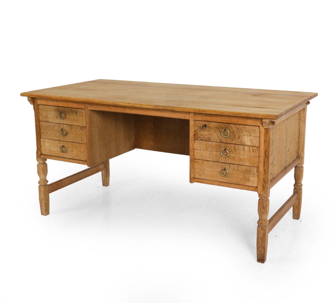 ATTR. HENNING KJAERNULF DANISH OAK DESK C. 1970S: Key included. Brass hardware and carved decoration to drawer fronts. Denmark, circa 1970s. Dimensions: H 29" x W 58" x D 30". Condition: Faint water rings. Wear consistent with age and use, including
