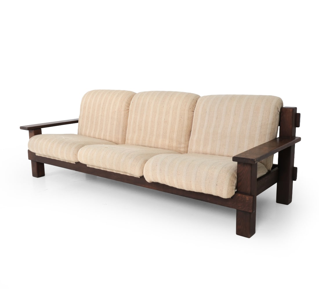 CARL STRAUB STYLE GERMAN OAK SOFA C. 1960S: Beige striped cushions and stained oak frame. Germany, circa 1960s. Dimensions: H 31" x W 87" x D 33" x SH 16" Condition: Showing signs of wear including soiling, fading. Tears and fraying to