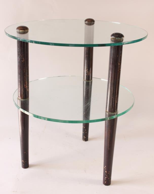 GILBERT ROHDE TWO TIER GLASS TABLE: Glass, lacquered wood Dimensions: Glass diameter 22" x H 24 1/2" Condition: wear to legs