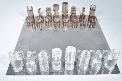 MICHEL DUMAS LUCITE CHESS SET: Lucite pieces on polished and brushed metal board, marked with Muchel Dumas sticker to boxDimensions: H 23.25" x W 23.25" (Board), H 10.25" x W 22.75" x D 3.75" (Pieces in case)Condition: overall