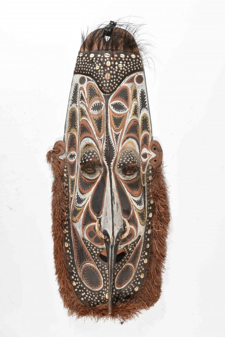 NEW GUINEA IMBRANDO SPIRIT MASK: Carved wood, grass, painted pigments and cowrie shells. Dimensions: H 43" x W 17.5" Condition: Some loss of shells, cracks to wood