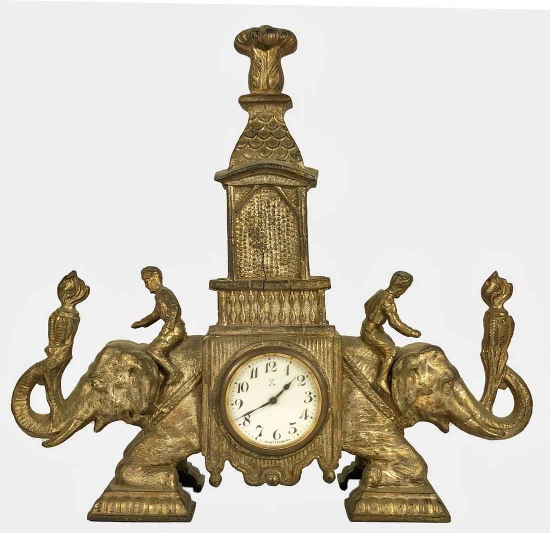 Elephant-Form Table Clock: Cast metal table clock with kneeling elephants. German clock movement. Circa 1900. W. 12 1/2 inches. H. 11 1/2 inches. D. 3 1/4 inches.