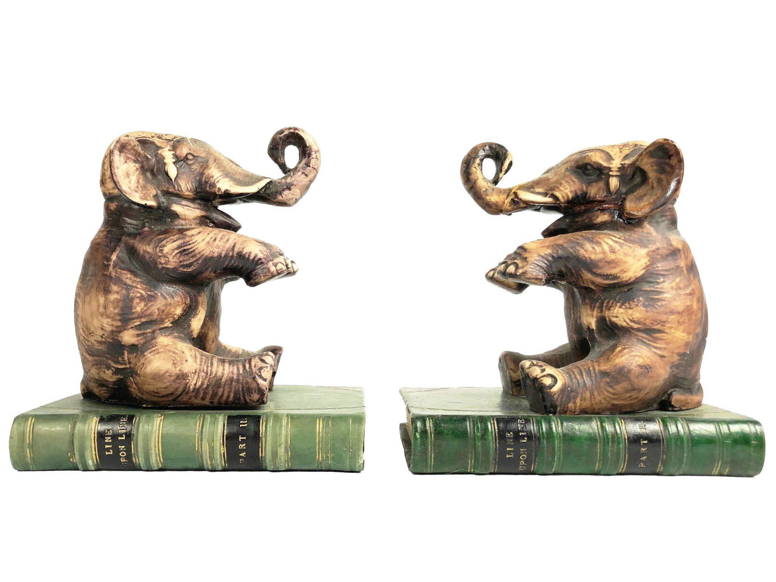 Pair Elephant-Form Bookends: Pair of painted ceramic bookends, each in the form of an elephant seated atop a book. Circa mid-20th century. L. 5 inches. H. 5 1/2 inches. Chip to one base; one of the elephant trunks appears to have