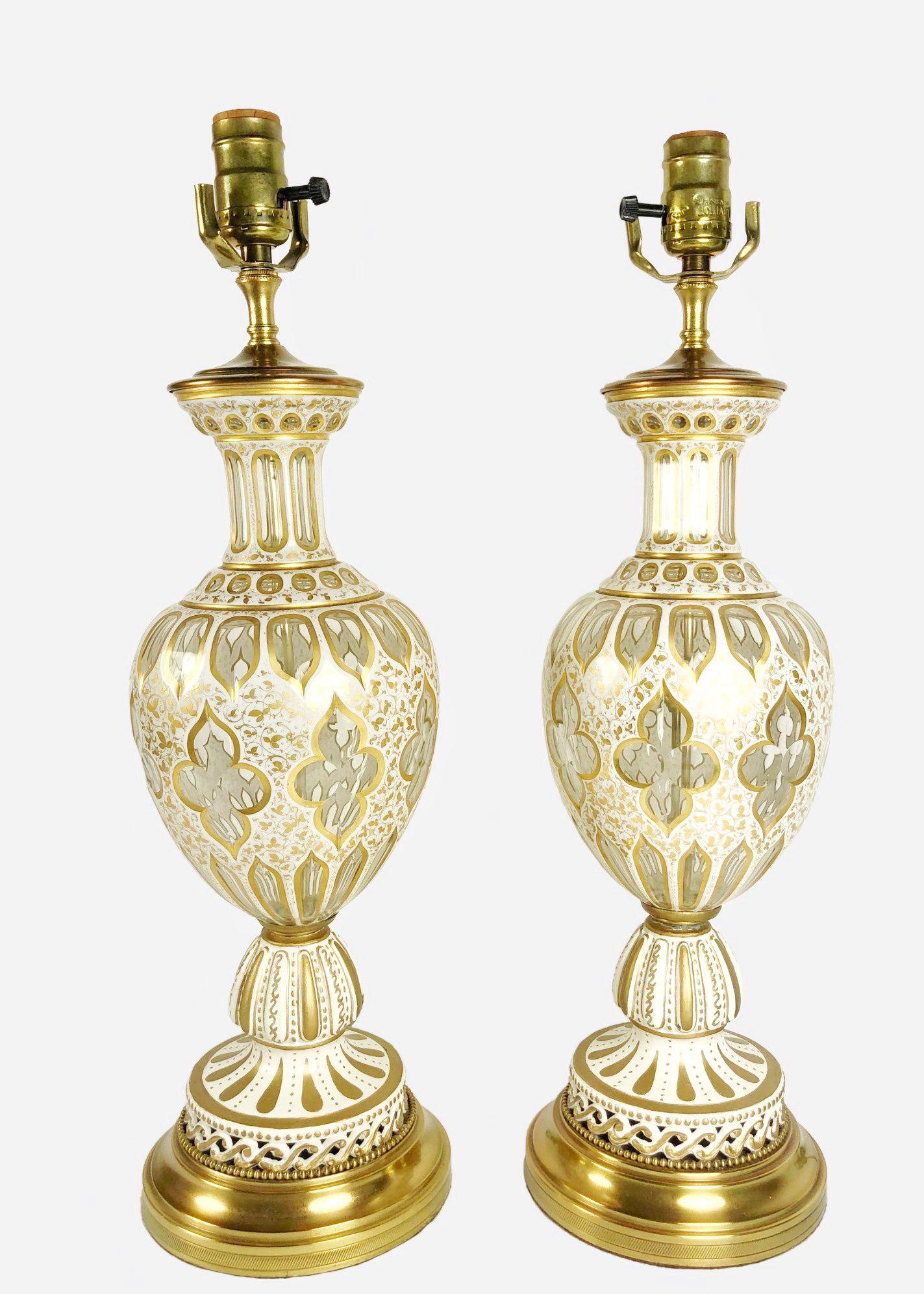 Pair Of Overlay Glass Lamps, Circa 1940: Vintage pair of urn-form cut overlay glass lamps, opaque white to clear glass, gilt highlights; European, possibly French, circa 1940. H. 17 inches. (Harps, including faceted crystal finials, 12 inche