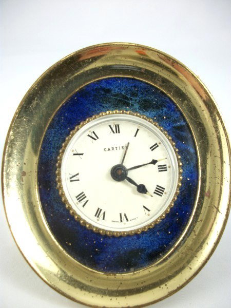 Cartier Bedside Alarm Clock: Faux lapis face inside an oval brass ring, round white dial with black Roman numerals, easel back. Circa mid-20th century. H. 3 1/4 inches. Overall very good condition; some scratches and pitting to b
