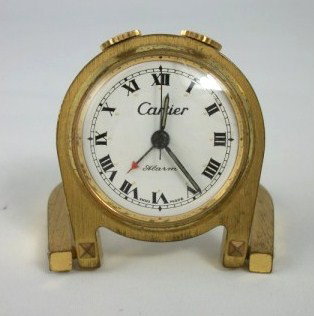 Cartier Travel Alarm Clock: Double "horseshoe" design, white dial with black Roman numerals, signed Cartier. Circa mid-20th century. Overall good condition; some scratches and wear to brass case. H. 1 1/2 inches. W. 1 3/4 inches