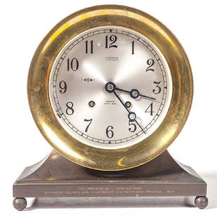 Chelsea Ship's Bell Clock: Round brass clock manufactured by Shreve Crump and Law Company. Engraved to front of base. Clock rests on metal footed base. Working condition, No key. 8 1/2w x 3 1/2d x 9 1/4h.