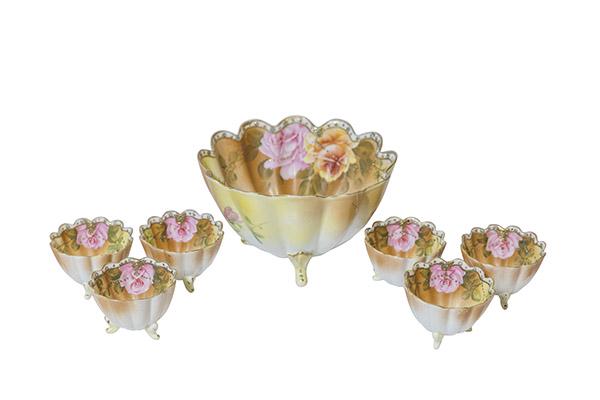 Three Footed Nippon Nut Set With Roses: Seven piece Nippon Nut set with hand painted pink and yellow roses with green leaves. Motif with moriage and jeweled trim with gold beading draped around the roses. Bowl and cups with scrolled three f
