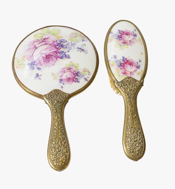 Porcelain Hand Mirror and Brush Set: Antique Victorian hand mirror and hair brush vanity set. Painted roses and violets on white enamel with brass floral embossed handles and beveled mirror. Mirror 5 1/4" W x 9 1/2" L Brush 2 3/4" W x 8 