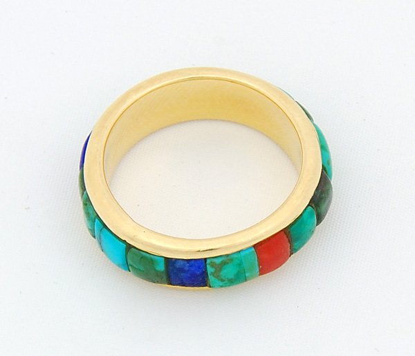 Charles Loloma Gold Ring: Charles Loloma consisting of flat circular setting with flange protrusions on each side, outer surface aligning a series of 5 stones of varying colors including lapis, turquoise, and coral set in yell