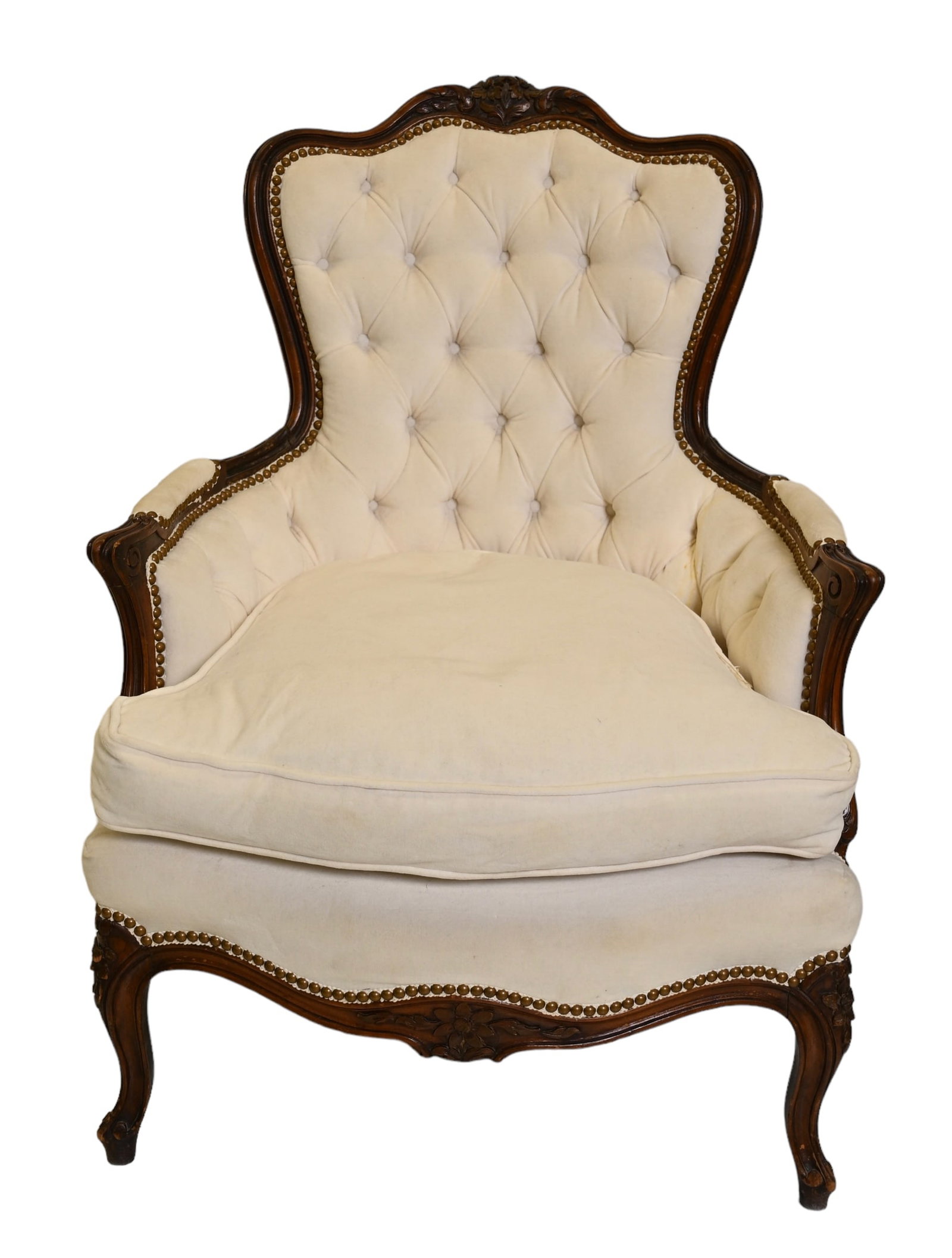 Carved French Bergère: Carved French Bergère. 20th century. Sculptured crest rail and carved arms with tufted upholstery. Scalloped walnut aprons with cabriole legs resting on hoof feet. Brass studded trim and mohair uphol