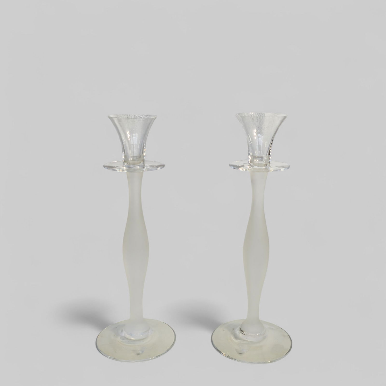 Orrefors Celeste Frost Crystal Glass Candle Holder: Pair of crystal frost glass candlesticks designed by Anne Nilsson for Orrefors Celeste. Candle holder is made of hand blown crystal glass and has a frosted slender stem with clear flared top. 4 1/2h x