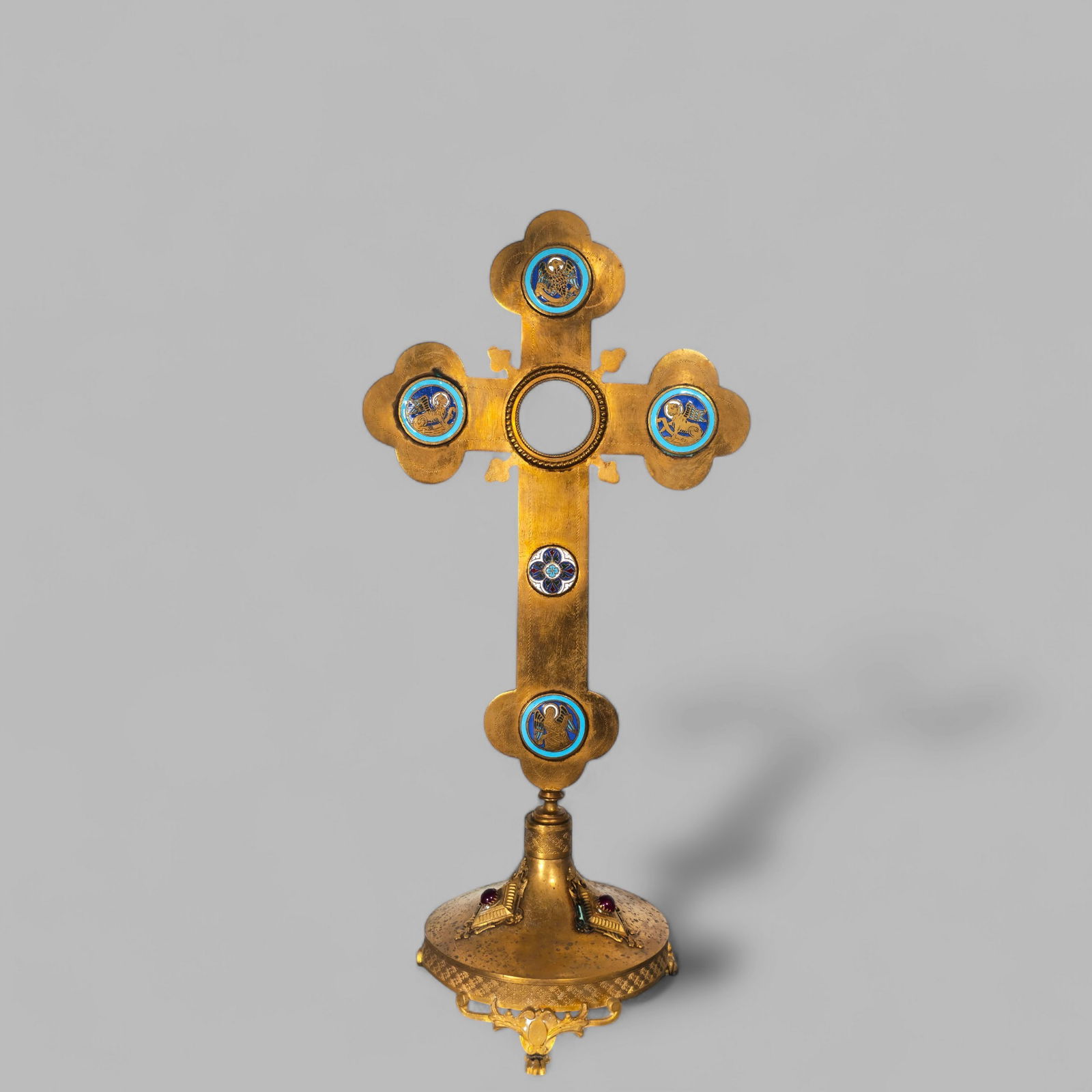 Gilt Bronze Reliquary Cross: Gilt Bronze Reliquary Cross. Gilt bronze free-standing cross with enamel plaques. Center opens for relics. Round footed base with paw feet. Three high relief diamonds with embedded jewels. 5 1/2w x 5