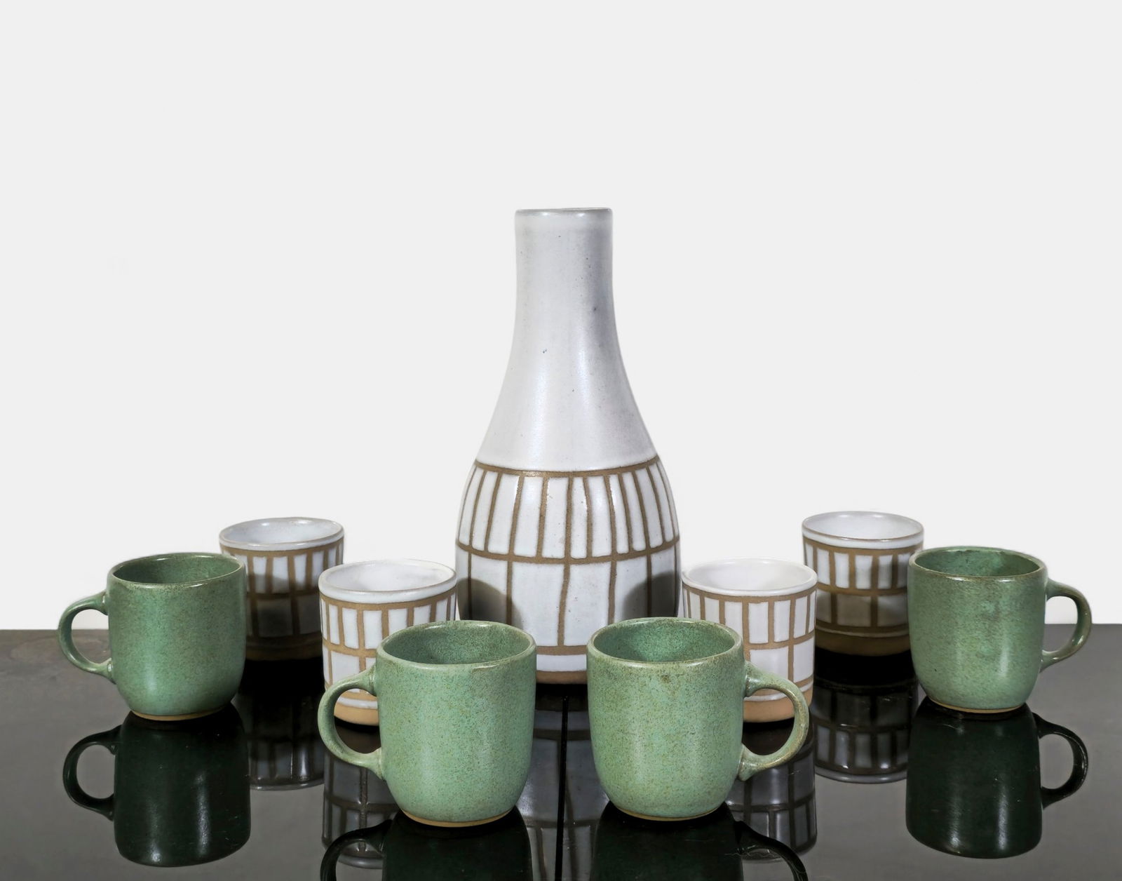 Gordon & Jane Martz Carafe Plus: Mid-century modern stoneware beverage set by Gordon and Jane Martz, including a tall carafe with incised grid decoration and six coordinating mugs in matte green and taupe glazes. Exemplifies the Mart