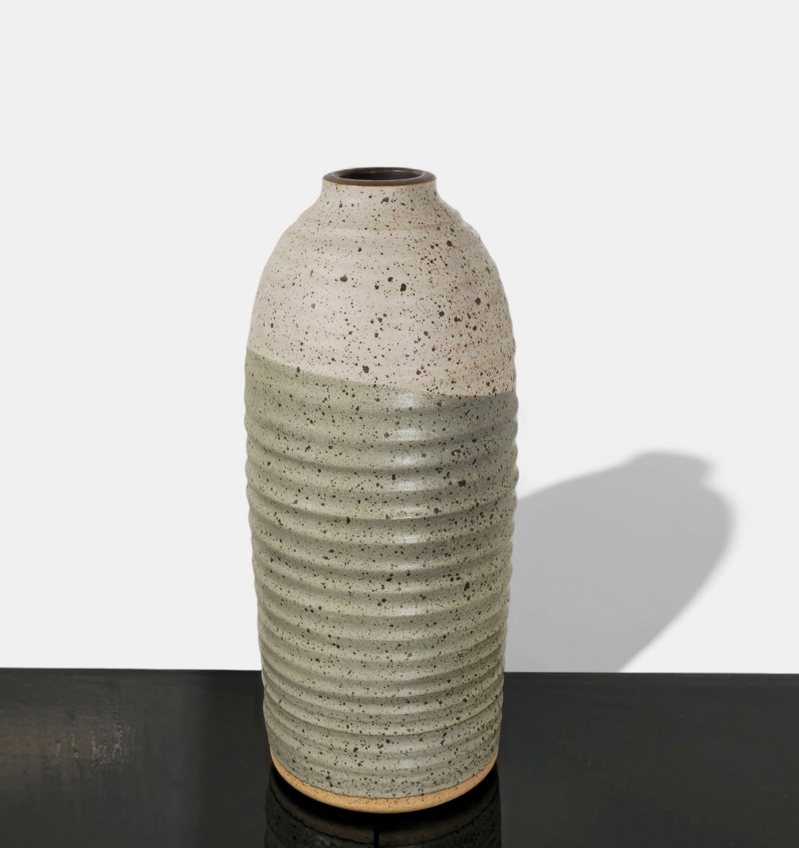 Alvino Bagni Stoneware Vase: Mid-century Italian stoneware vase by Alvino Bagni with a ribbed cylindrical body and contrasting upper portion glazed in speckled off-white. The lower half is smooth, rendered in a muted sage-green g