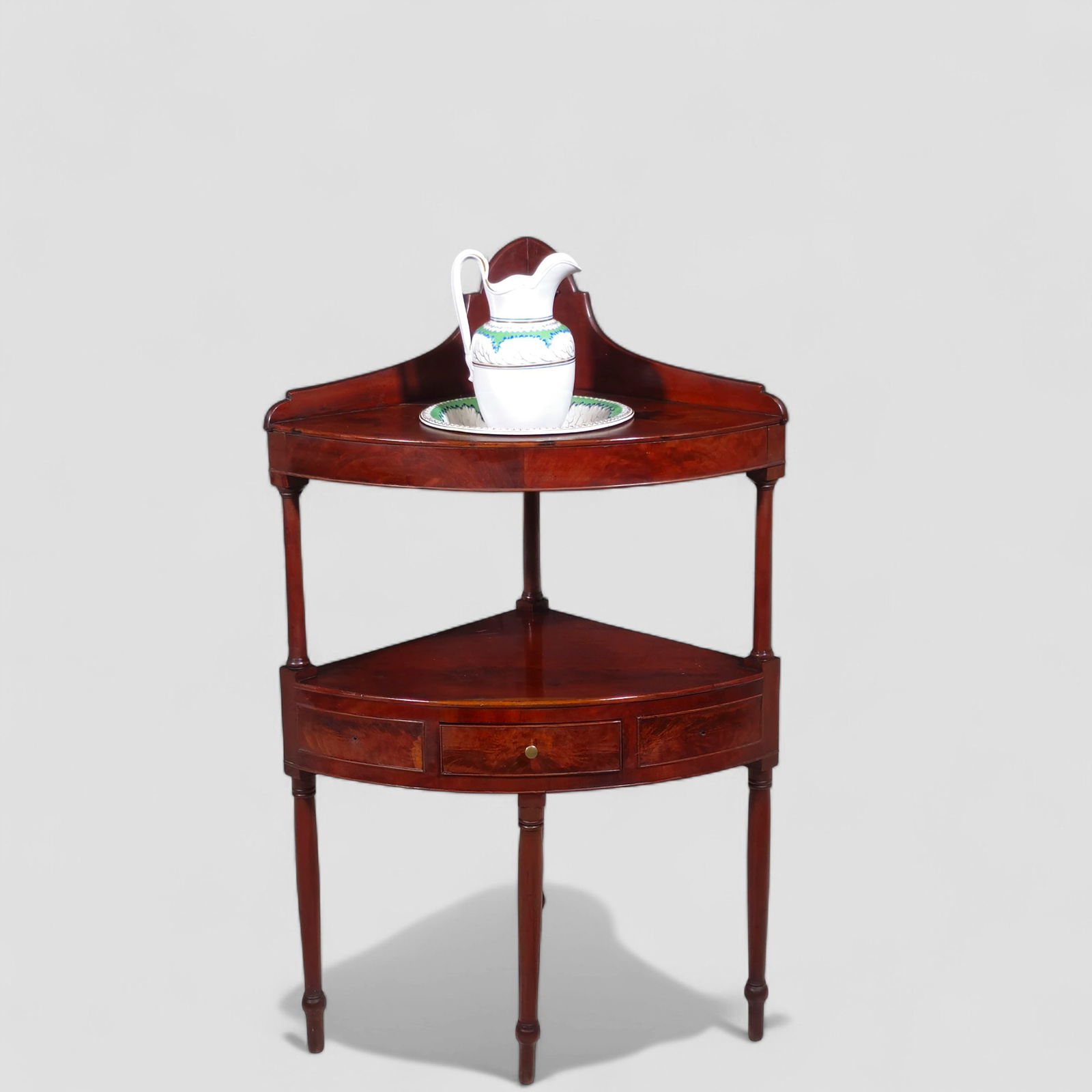 18th Century Georgian Mahogany Corner Washstand: 18th Century Georgian Mahogany Corner Washstand. Circa 1780-1810. Curved shaped back splash over a curved top and apron. Original porcelain wash basin and pitcher. Lower shelf above an single center d